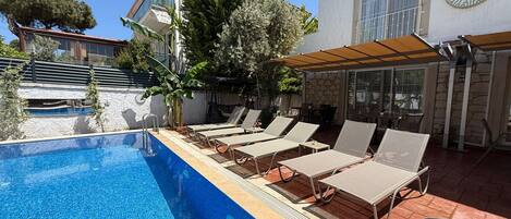 Una piscina con sillones de descanso, un porche cubierto y un edificio con un cartel que dice 'REBETIKO'.
