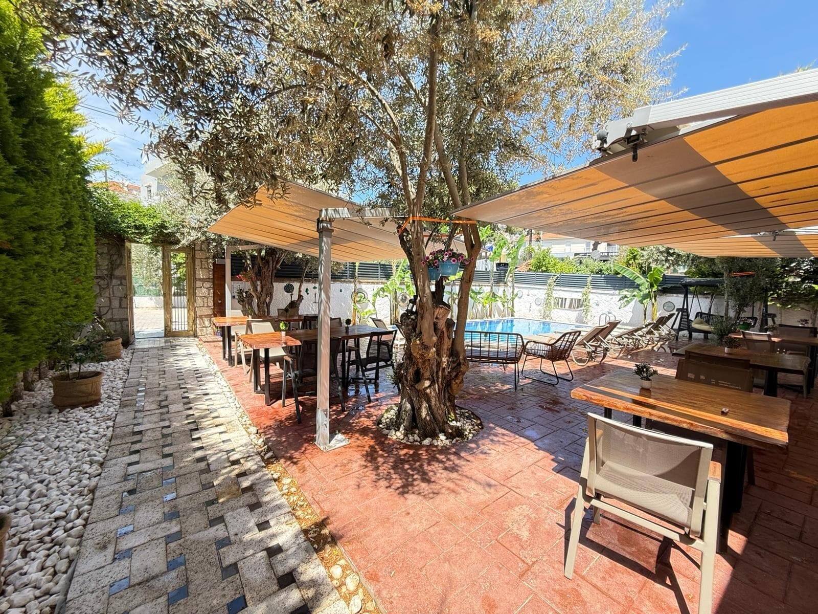 Ein Außenbereich mit Terrasse, Tischen, Stühlen, einem Schwimmbecken und einem gepflasterten Weg.