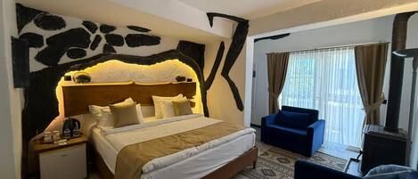 A hotel room with a bed, a nightstand, a blue armchair, a window with curtains, and a fireplace.