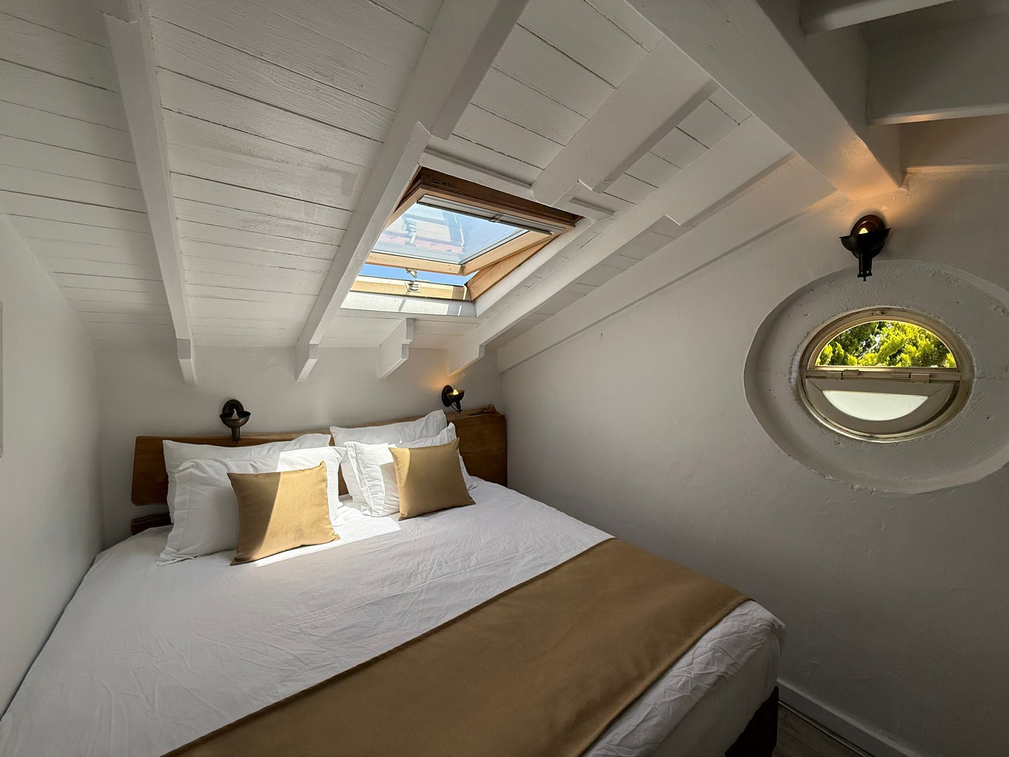 A bedroom with a skylight, a round window, and a bed with pillows.