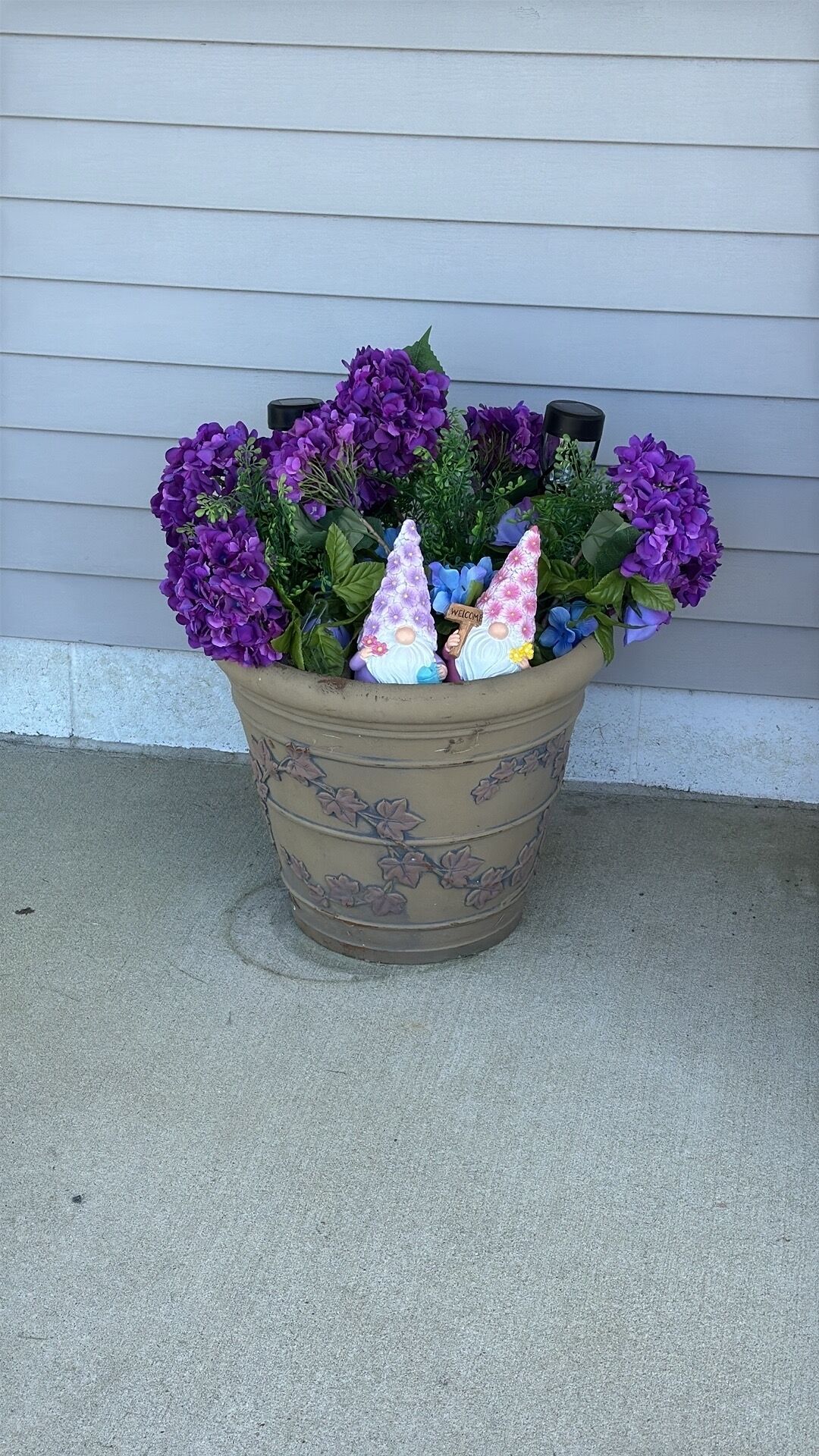 A potted plant with purple flowers and two decorative figures on a concrete surface.