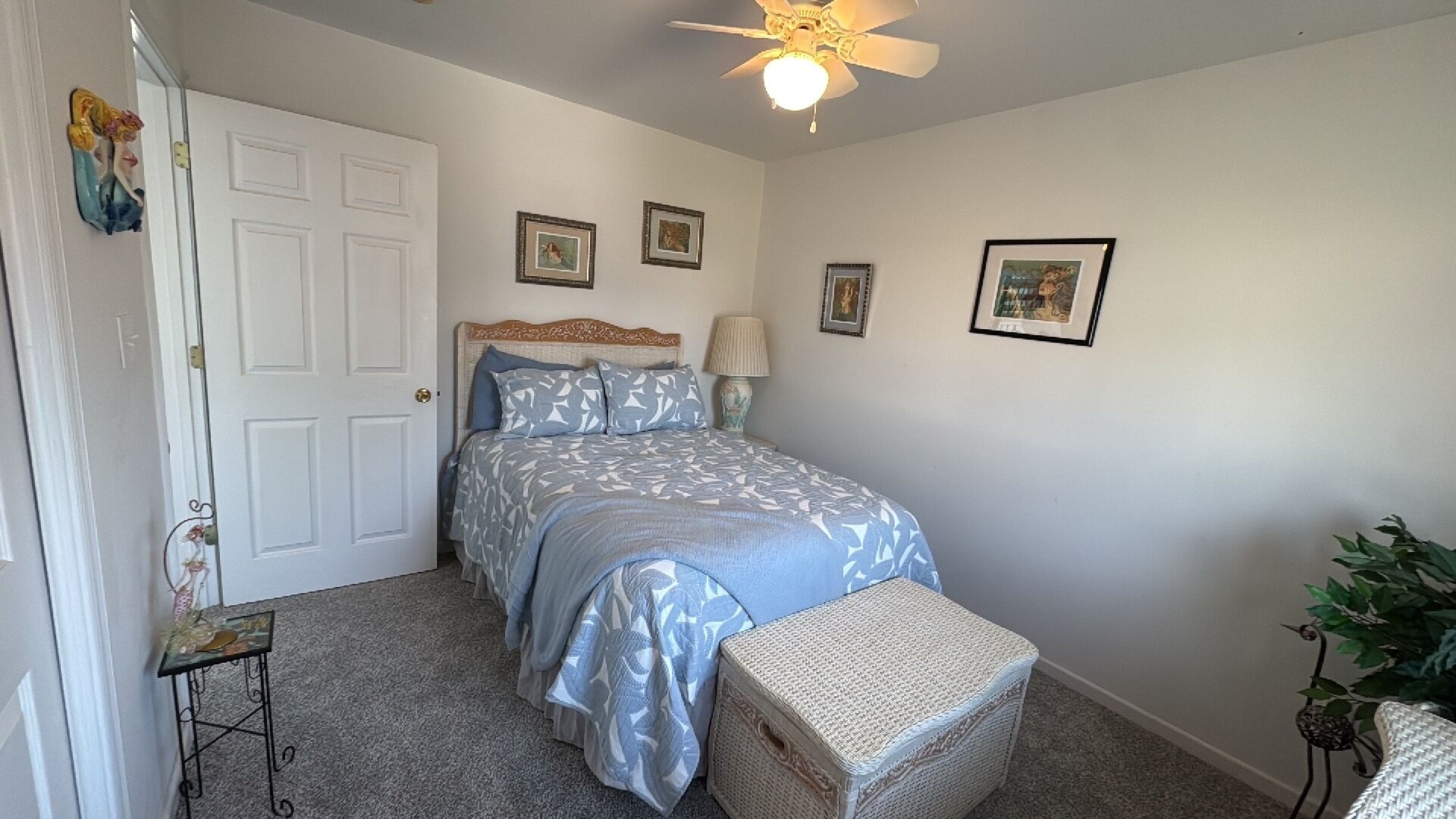 Camera da letto con un letto, una ventola a soffitto, un comodino, una lampada e quadri appesi al muro.