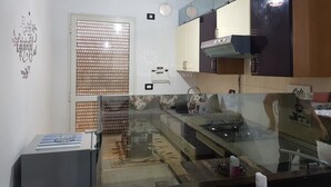 Eine moderne Küche mit Einbauofen, Mikrowelle und Herd. Es gibt ein Fenster mit Jalousien, eine Deckenleuchte und ein dekoratives Wandelement.
