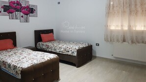 Ein Schlafzimmer mit zwei Betten, floralem Bettzeug, einer Wand mit Mohnbildern und einem Fenster mit durchsichtigen Vorhängen.