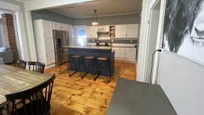 A modern kitchen with a central island, bar stools, and a dining area with a wooden table and chairs. - Meredith Charmer-walk to lake, town, shops, & boat launch (Meredith)