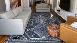 A living room with a sofa, ottoman, and a patterned rug. There is a television and a fireplace. - Meredith Charmer-walk to lake, town, shops, & boat launch (Meredith)