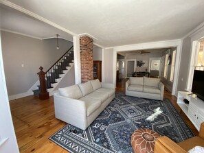 A spacious living room with a large gray sofa, a patterned rug, and a brick fireplace.