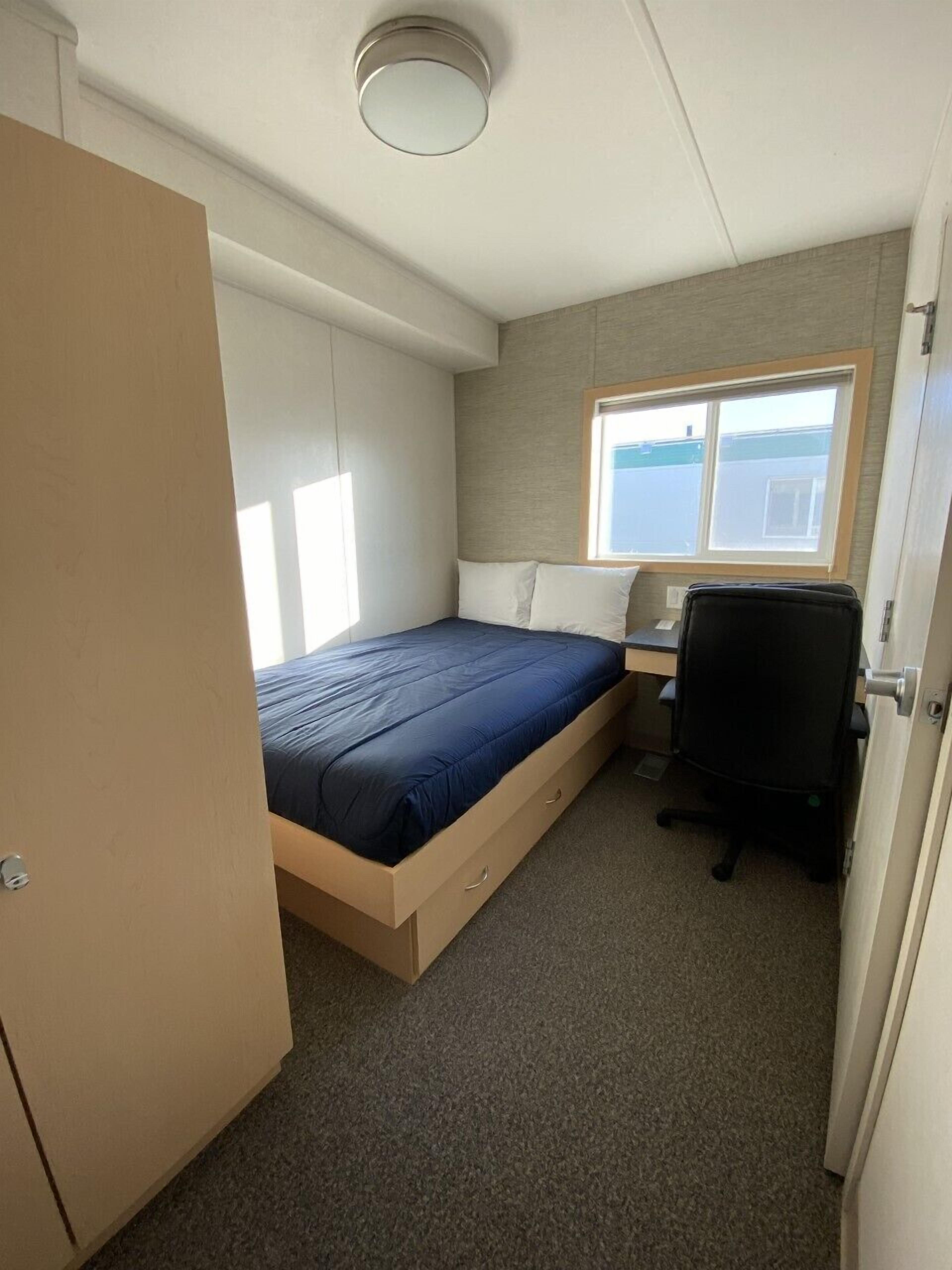 A compact room with a bed, a desk, and a chair.