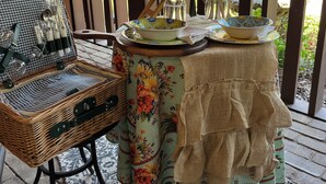 A covered outdoor seating area with a wicker chair, a table with floral tablecloth, and a decorative lantern. - Cedar Cottage Retreat with Mountain View’s  (El Cajon)
