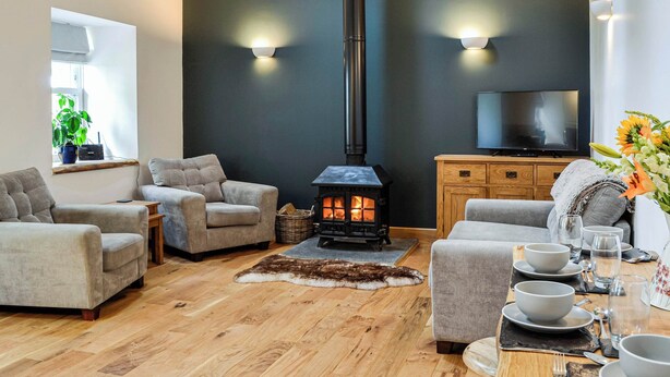 A cozy living room with a fireplace, sofas, a dining table set for four, and a television. - 2 bedroom accommodation in Kirriemuir (Kirriemuir)