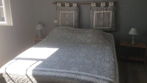 Ein Schlafzimmer mit einem Bett, zwei Nachttischen, einem Fenster und einem gerahmten Bild an der Wand.