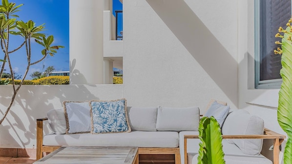 A modern outdoor seating area with a white sofa, striped cushions, and a wooden coffee table.