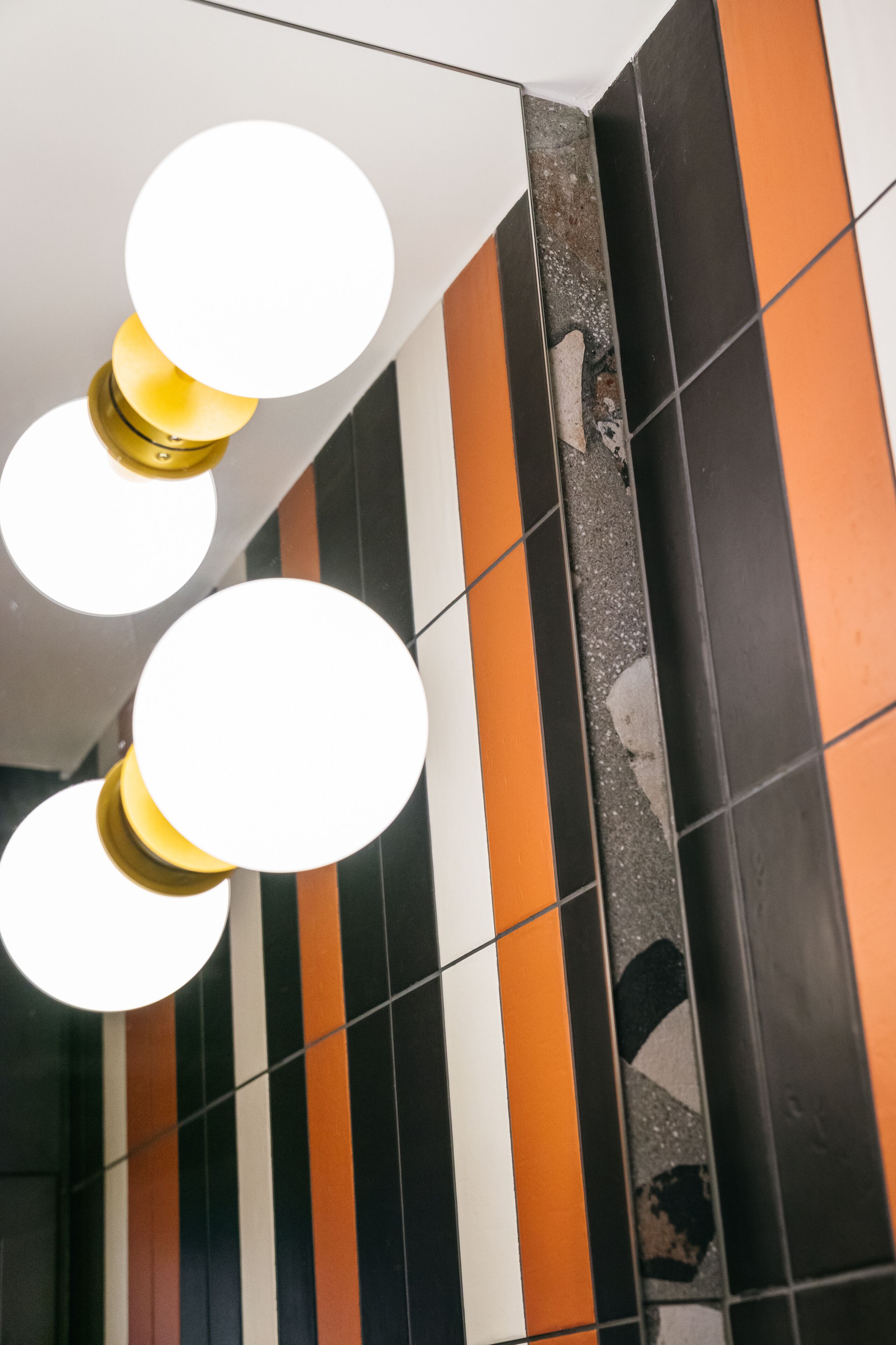 A corner of a room with a tiled wall featuring a striped pattern of black, white, and orange tiles.