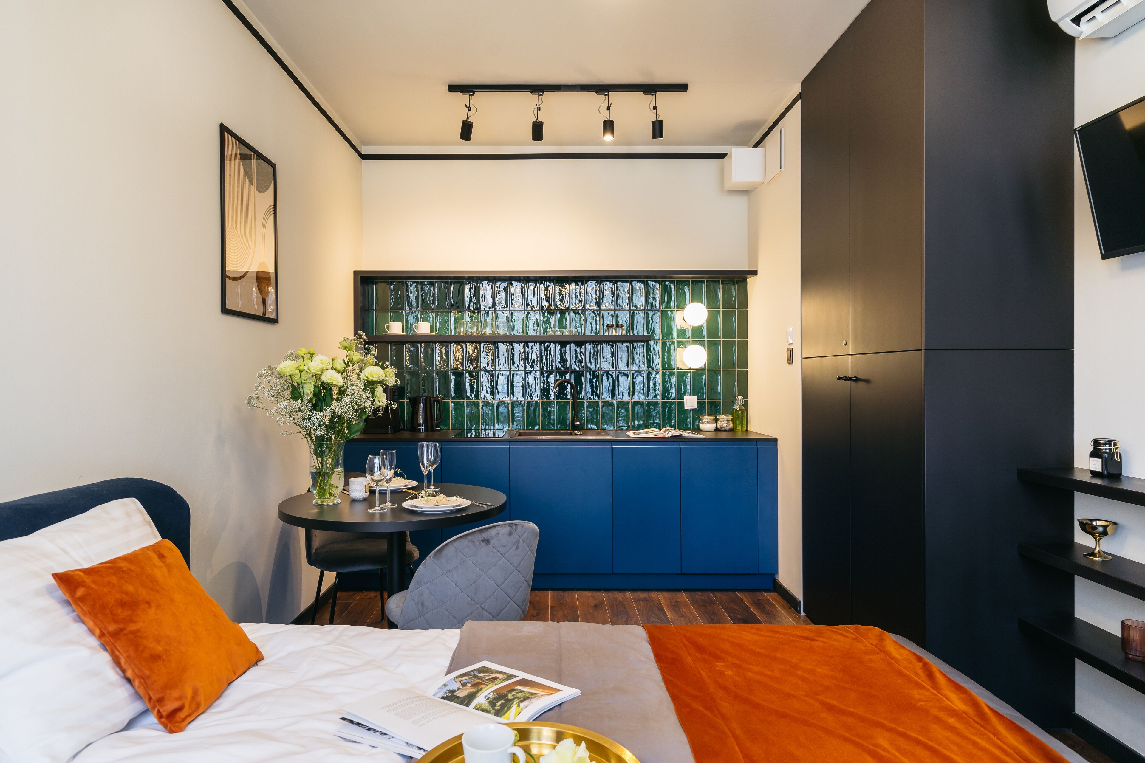 A modern hotel room with a bed, a small dining area, and a kitchenette.