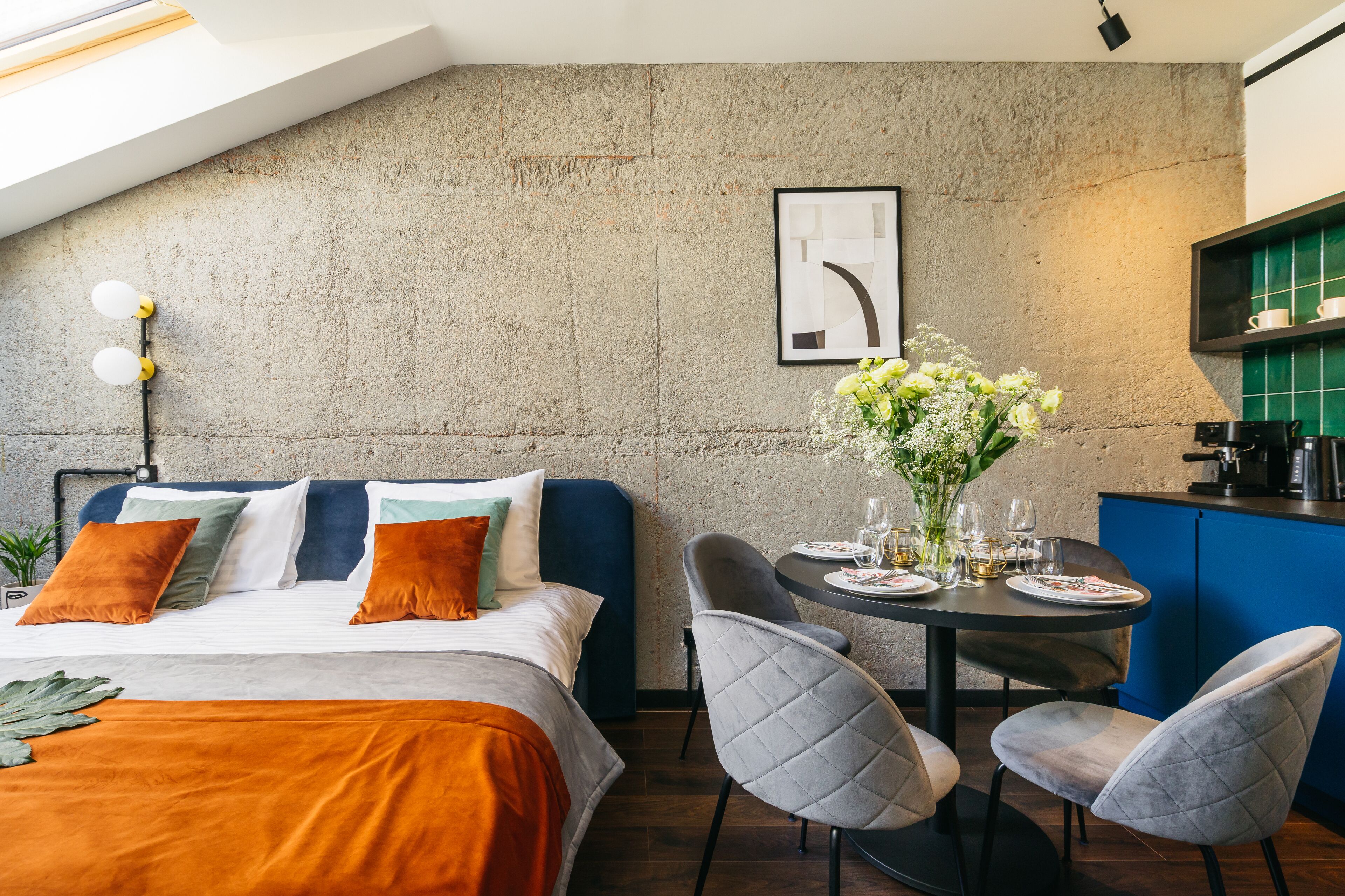A modern bedroom with a bed, bedside table, and a dining area with chairs and a table.