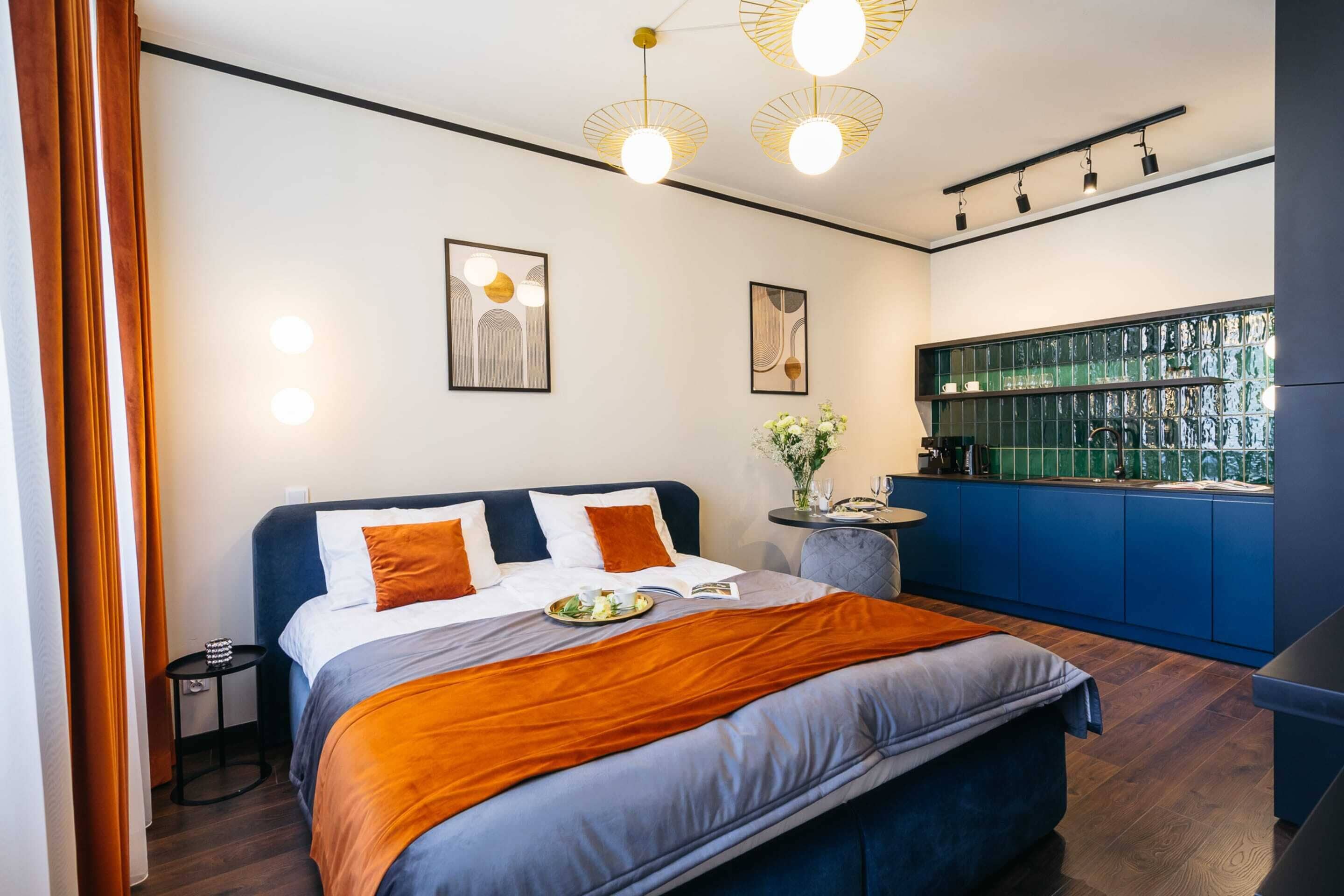 A modern hotel room with a large bed, a small side table, a bar area with shelves, and a view of the city through the window.
