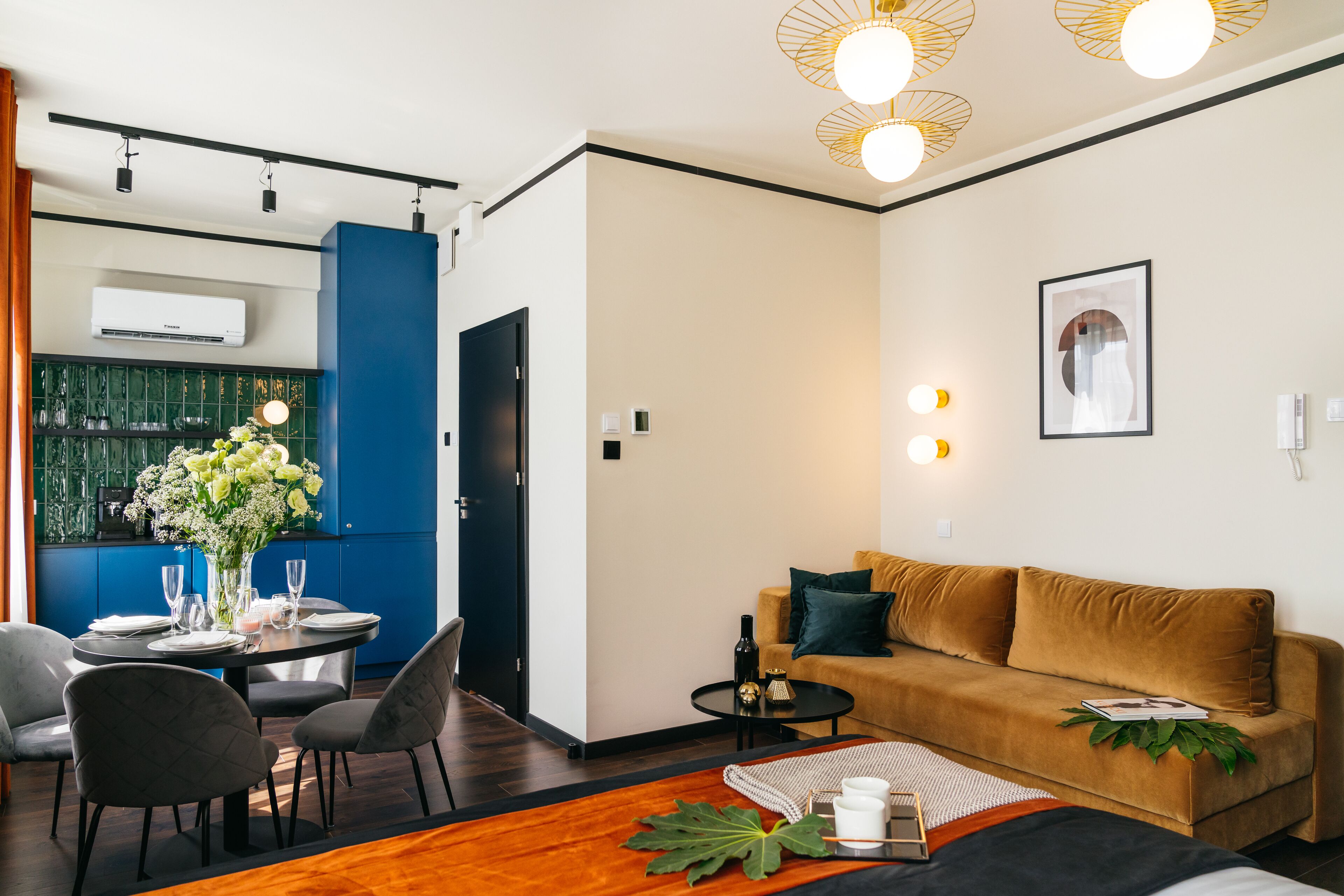 A modern living room with a sofa, a dining table with chairs, and a kitchen area in the background.