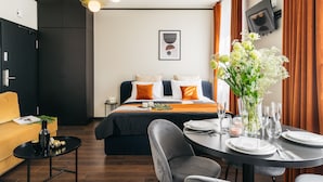 A modern hotel room with a bed, a dining table set for two, a sofa, and a small side table with a bottle and glasses. - Estery12 (Kraków)