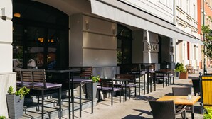 An outdoor cafe with tables and chairs, a stone wall, and a building entrance. - Estery12 (Kraków)