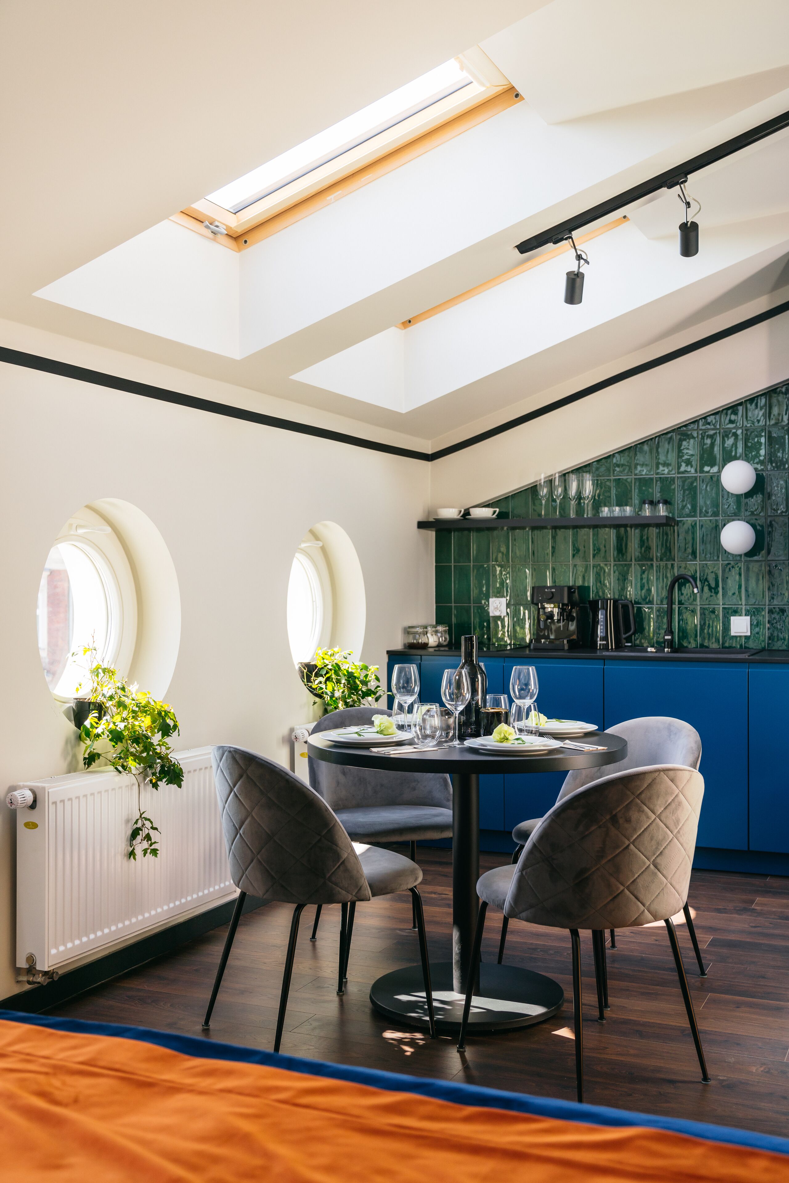 A modern kitchen with blue cabinets, a black countertop, and a skylight above the dining area.
