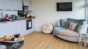 A modern kitchen with a dining area, a flat-screen TV mounted on the wall, and a cozy seating area with a sofa and cushions.