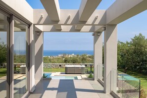 A modern outdoor patio with a hot tub, a pool, and a view of the sea.