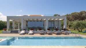 Un área moderna junto a la piscina con sillones de descanso y una zona de estar cubierta.