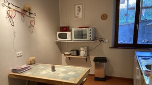 A compact kitchen with a wooden table, a microwave, a coffee maker, and a trash bin. - Meublé de tourisme in an old farmhouse for 4 people ( 2 stars) (Anould)