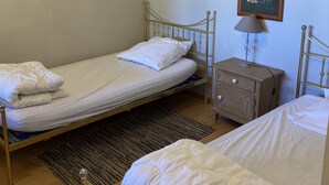 A bedroom with two single beds, a bedside table with a lamp, a small wooden dresser, a framed picture on the wall, and a chandelier. - Meublé de tourisme in an old farmhouse for 4 people ( 2 stars) (Anould)