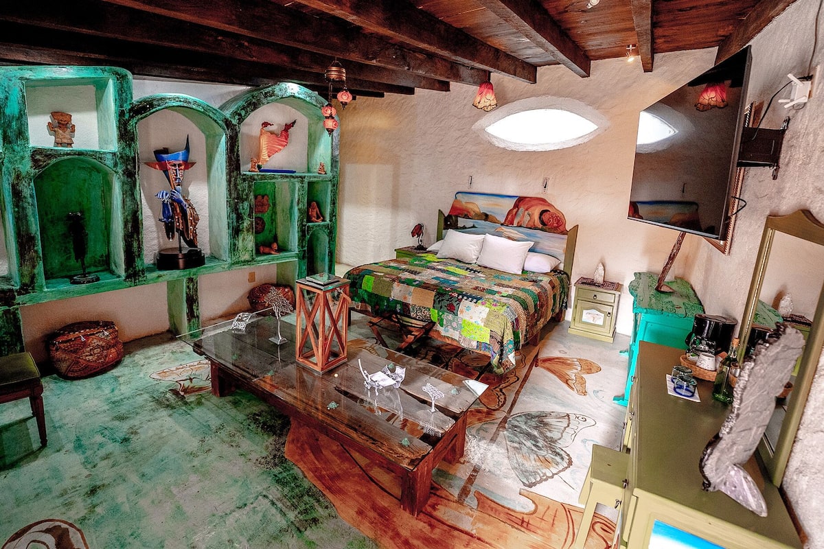 Ein rustikaler Raum mit einem hölzernen Bett, einem Glastisch und grünen Regalen mit verschiedenen Gegenständen.