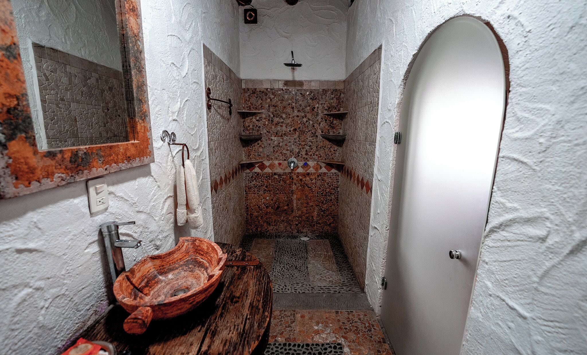 Un baño estrecho con diseño rústico, que incluye un lavabo de madera, un perchero y una zona de ducha con mosaicos.