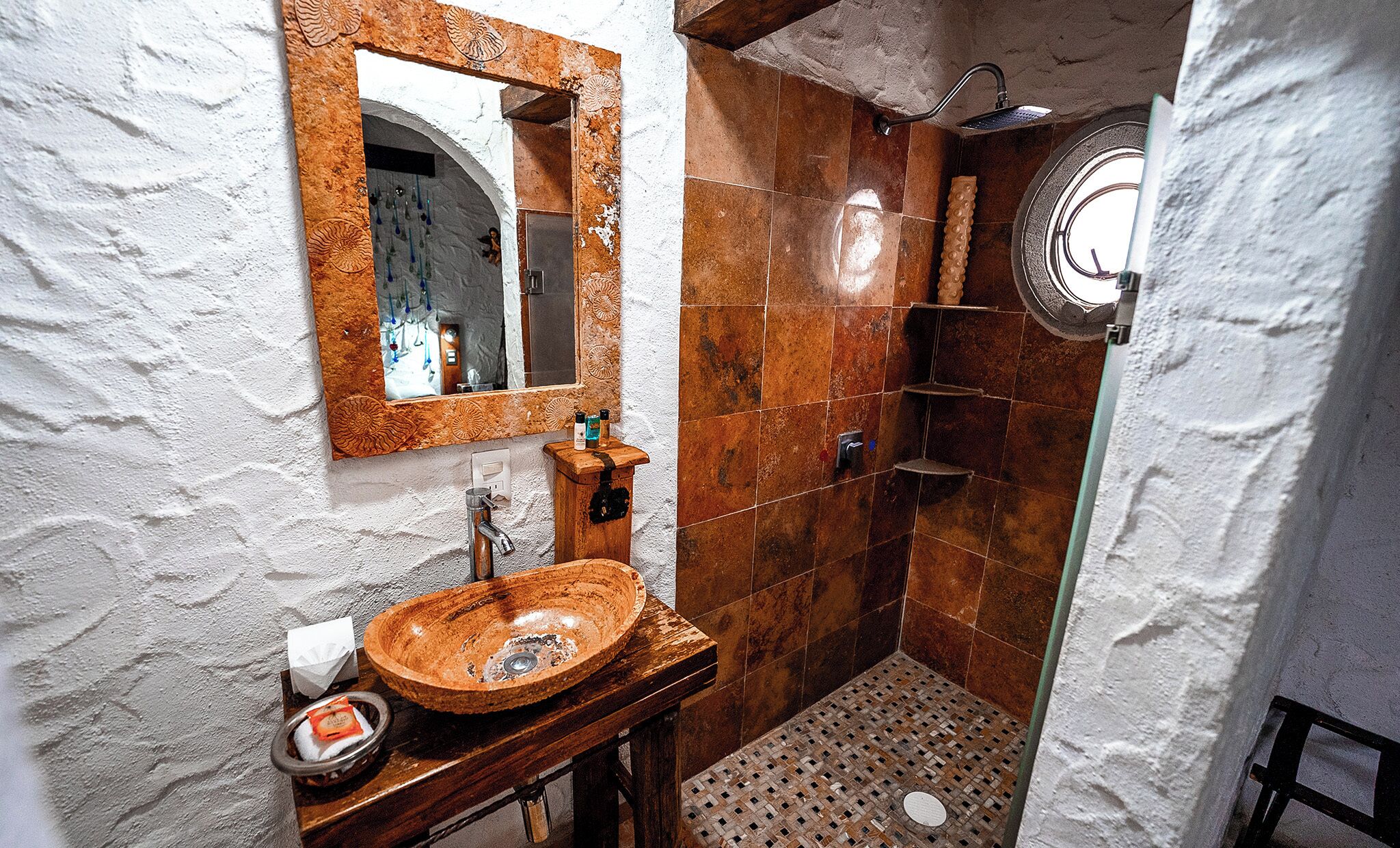 A bathroom with a wooden sink, a mirror with a decorative frame, a shower with a glass door, and tiled walls.