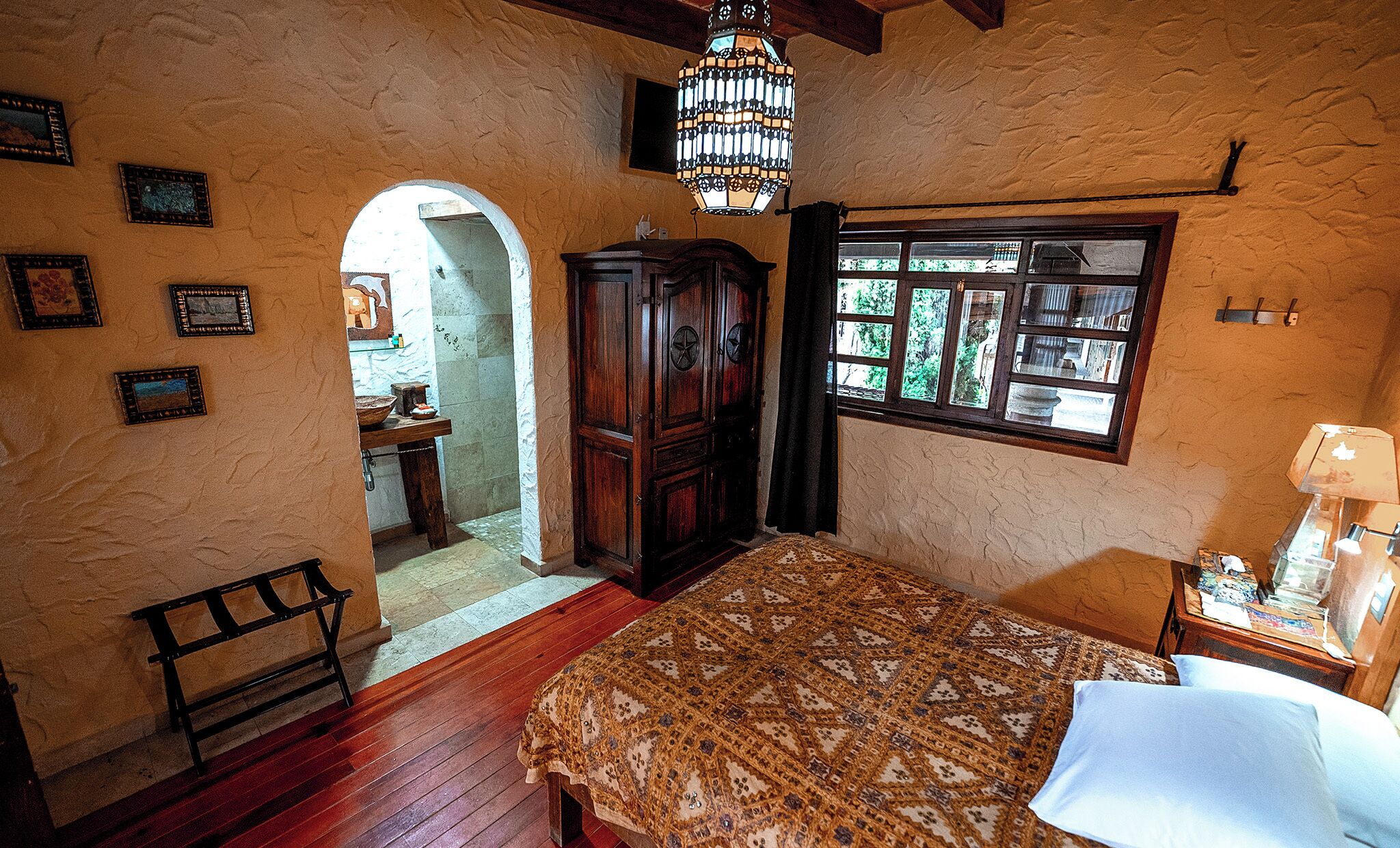 Ein Schlafzimmer mit einem hölzernen Bett, einem Nachttisch, einem Schreibtisch, einem Fenster mit Blick, einem Holzschrank und einer Chandelier.
