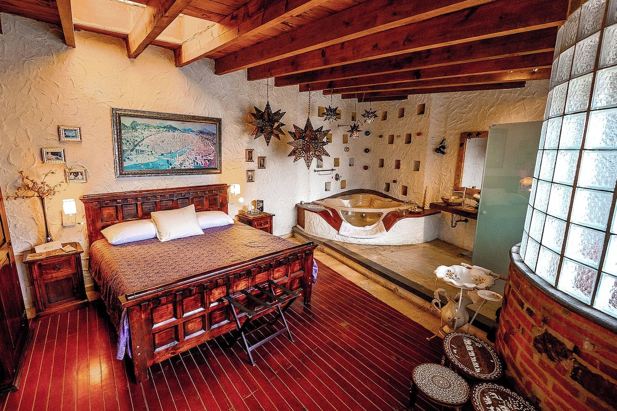 Ein Schlafzimmer mit einem hölzernen Bett, einem großen Gemälde, einer Badewanne und einer Steinwand.