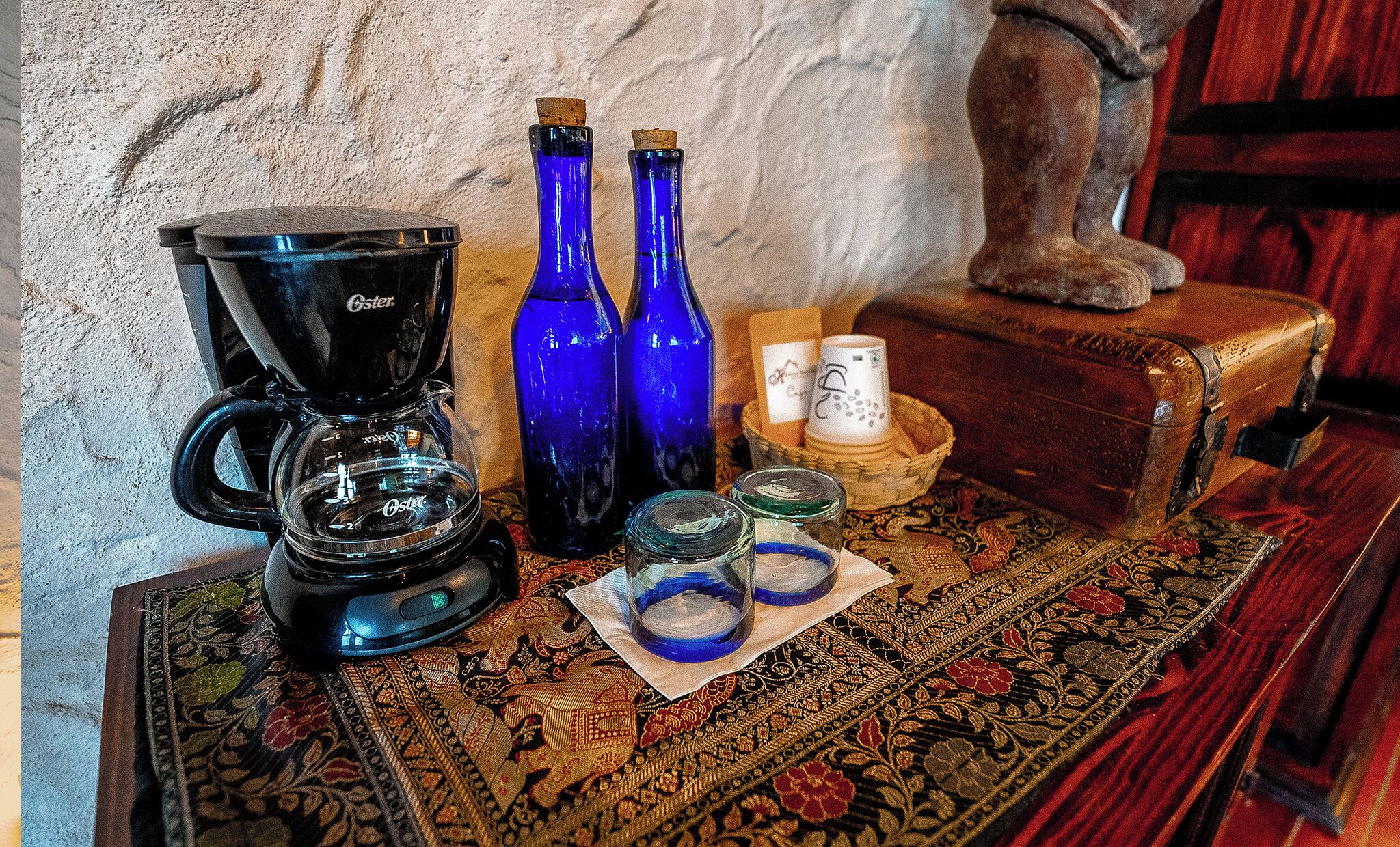Une machine à café, deux bouteilles bleues, des salières et des poivrières, et une boîte décorative posée sur une nappe à motifs.