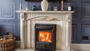 A fireplace with a white mantel, a mirror above, and a basket of firewood to the left. - 2 bedroom accommodation in Cluny, near Kirkcaldy (Cluny, near Kirkcaldy)