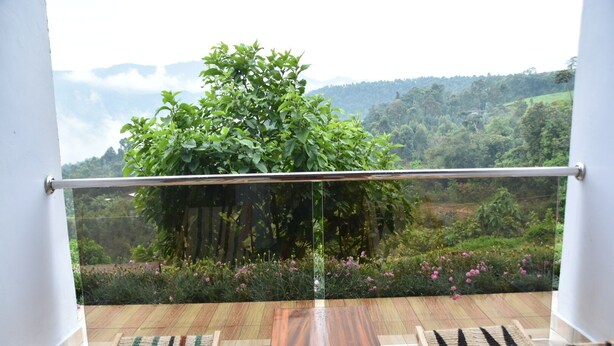 A balcony with a wooden floor, two wooden chairs, and a glass railing. - Chimpanzee Lodge (Bushekeri)