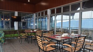 A restaurant with multiple tables and chairs, large windows, and a television screen. - Chimpanzee Lodge (Bushekeri)
