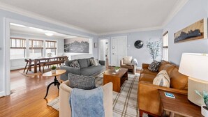 Un salón amplio con un sofá gris, un sofá de cuero marrón y una zona de comedor con mobiliario de madera.