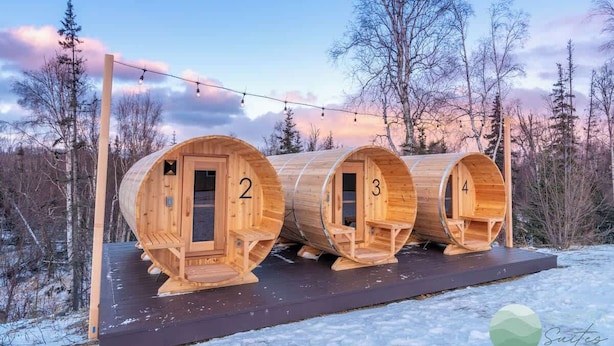 Cuatro cabañas sauna de madera, numeradas 2, 3 y 4, con una terraza de madera al frente.