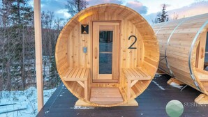 Una cabaña de madera con diseño circular, número 2, con puerta de cristal y asientos tipo banco en su interior.
