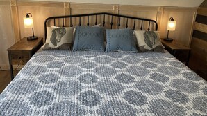 A neatly made bed with patterned bedding, two bedside lamps, and a headboard with a decorative design. - Unique Experience and Stay on a Working Alpaca Ranch. (Lincoln)