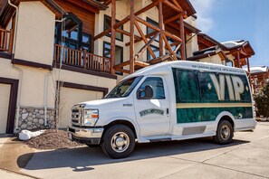 Un autobus navette blanc, arborant le logo « Resort Group », est garé devant un bâtiment doté de balcons en bois et d’une fondation en pierre.