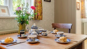Una mesa de comedor con vajillas azules y blancas, arreglos florales y scones.