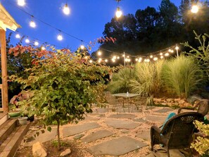 An outdoor patio with stone flooring, string lights, and various plants. - Guesthouse (Crozet)