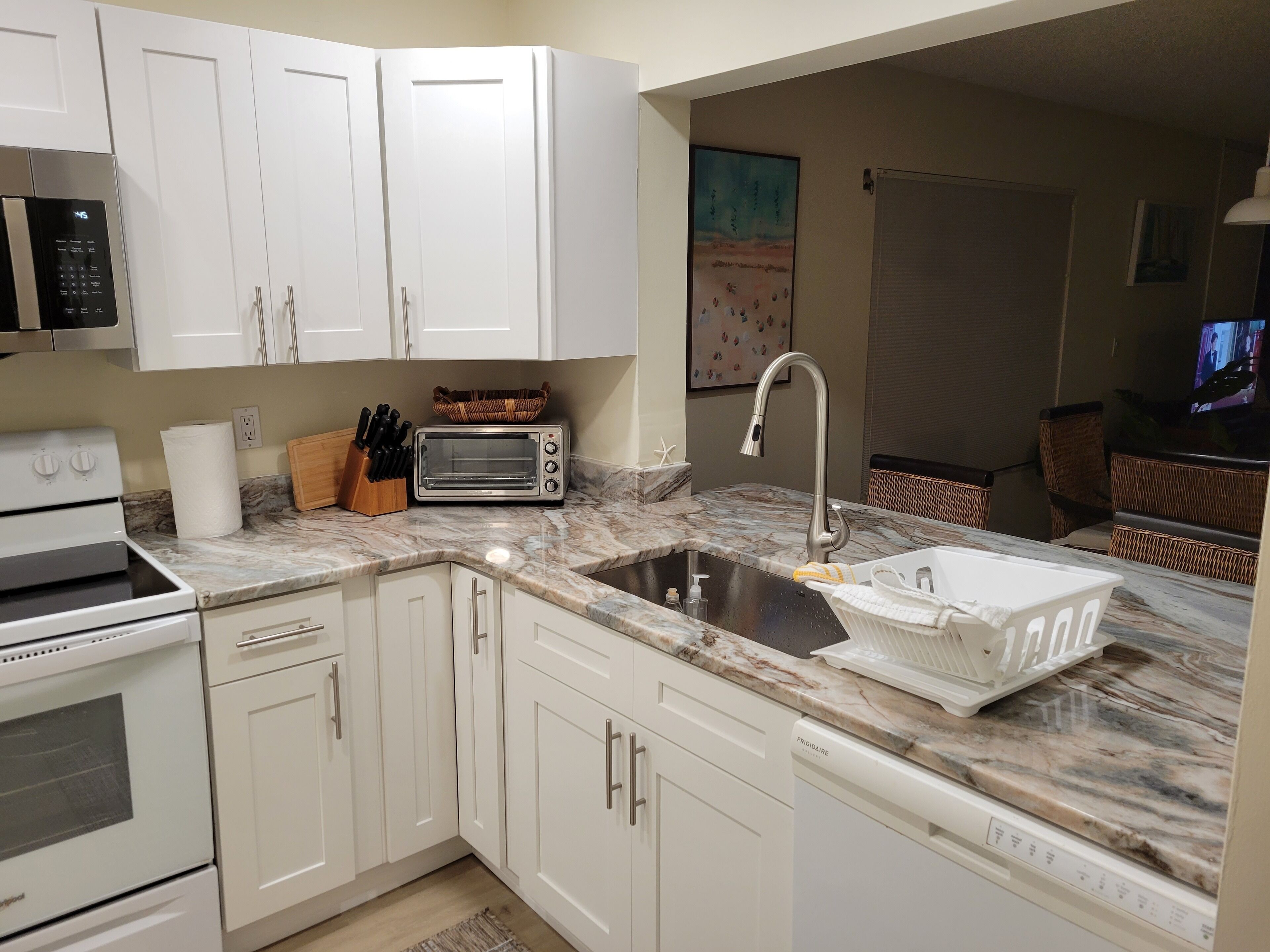 A modern kitchen with white cabinets, a built-in oven, a microwave, a toaster, and a sink with a dish rack.