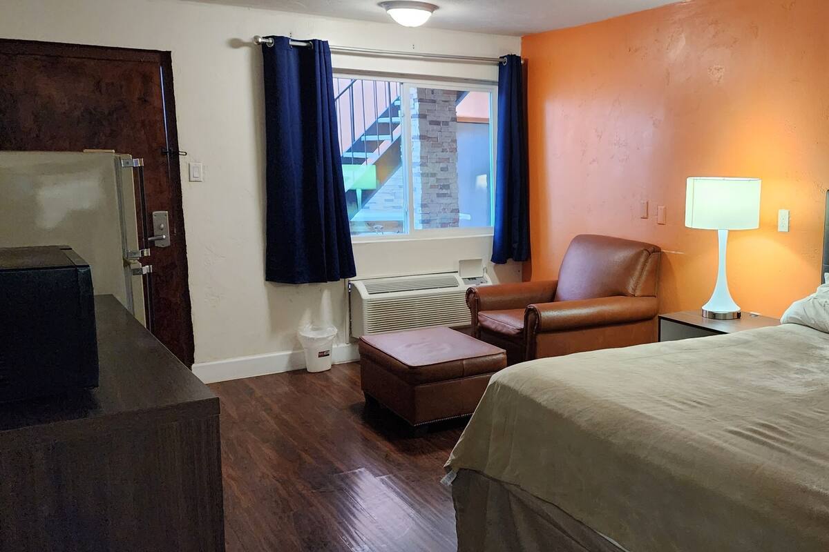 Une chambre d’hôtel avec un lit, une chaise, un bureau et une fenêtre avec des rideaux.