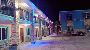 A multi-story building with a covered outdoor area, a staircase, and a parked vehicle. - B&J Hotel and Apartment (Pecos)