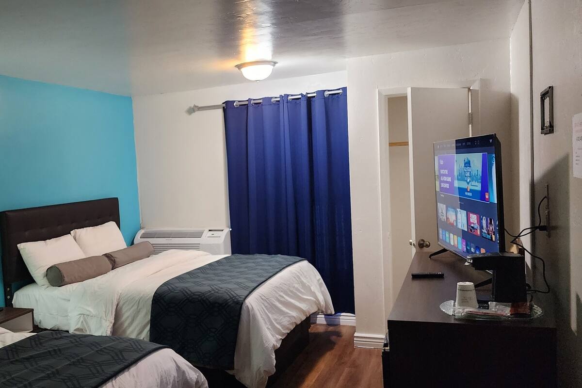Une chambre d’hôtel avec deux lits, une télévision, un bureau avec une machine à café et une salle de bain avec un rideau de douche.