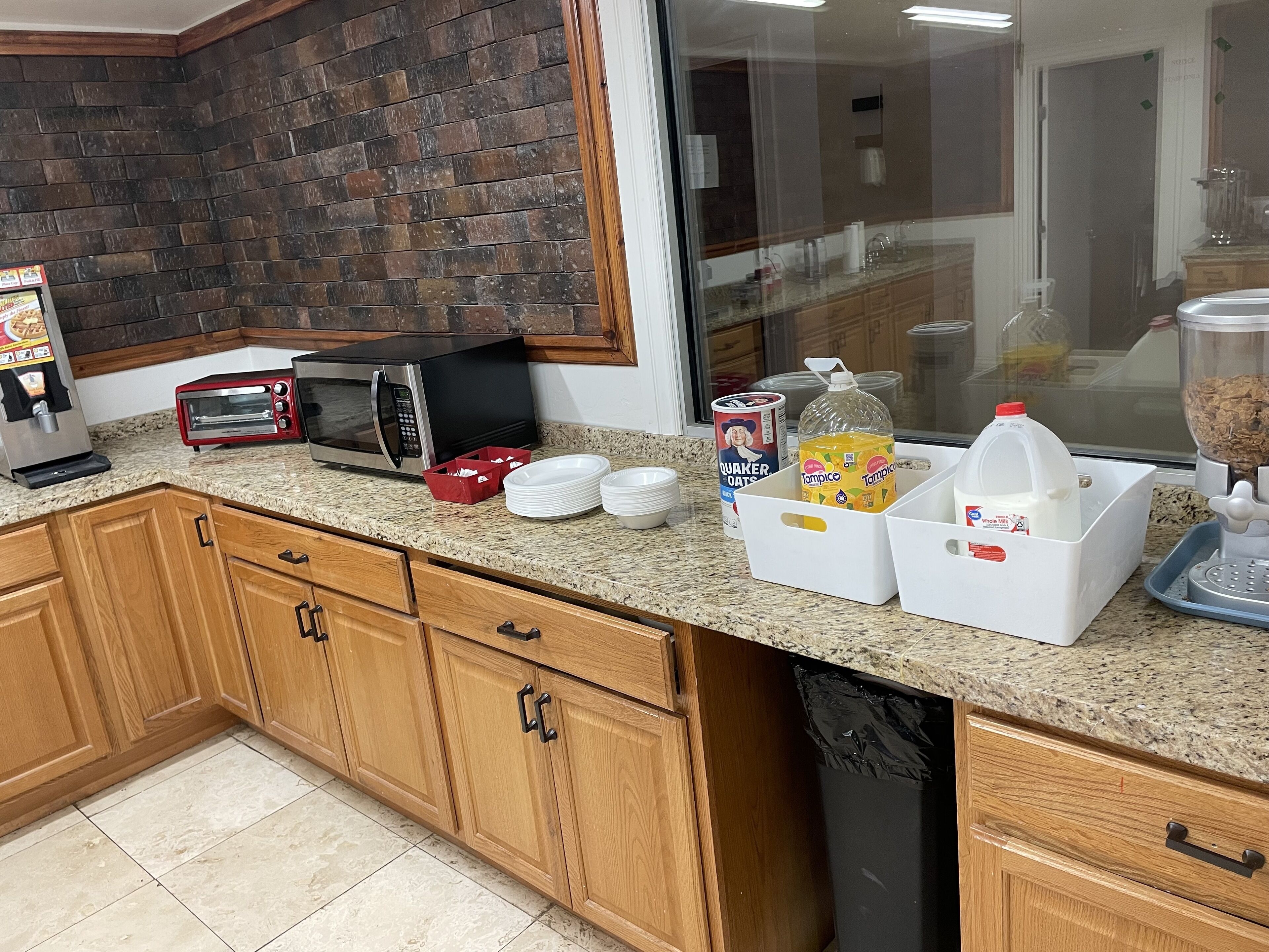 A kitchen with granite countertops, wooden cabinets, a brick backsplash, and various appliances including a microwave, toaster, and coffee machine.